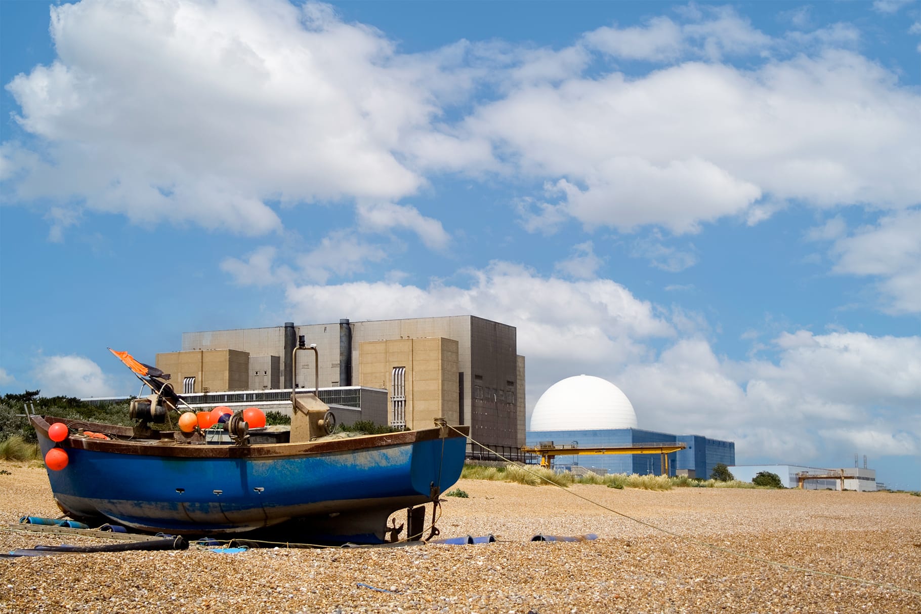 Blue fishing boat on a pebble beach with Sizewell C nuclear power station in the background.