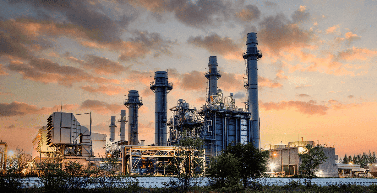 Combined cycle power plant at dusk with chimneys and illuminated structures.