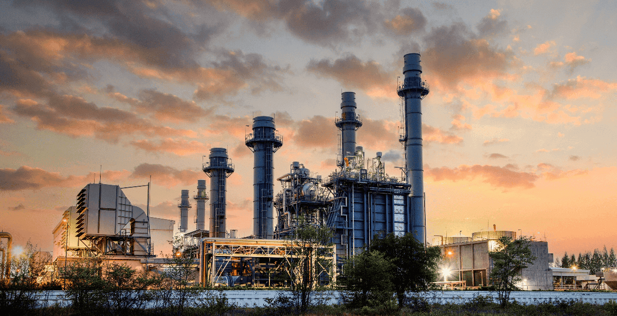 Combined cycle power plant at dusk with chimneys and illuminated structures.