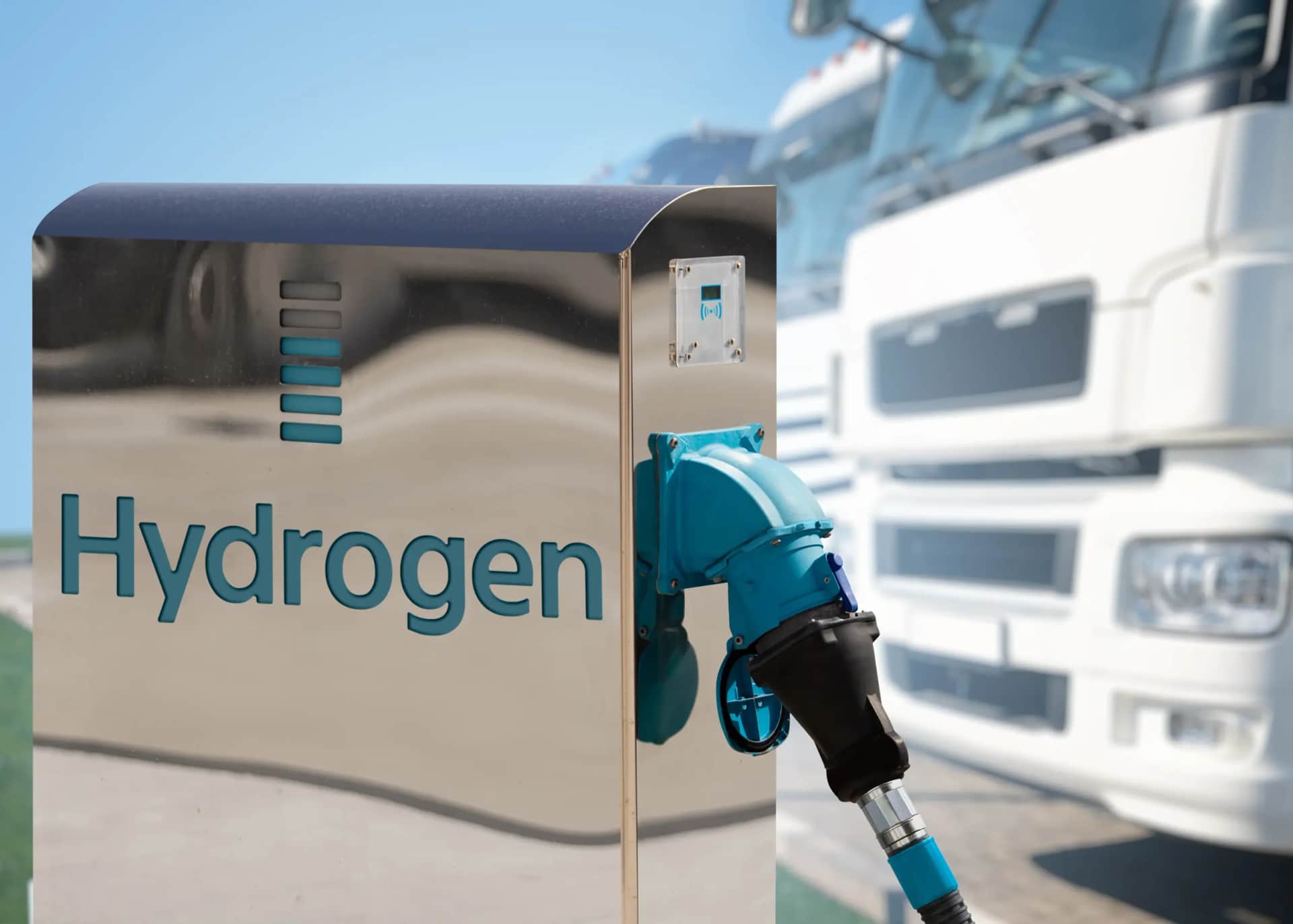 Hydrogen refueling station with metallic dispenser, blue writing, and trucks in background.