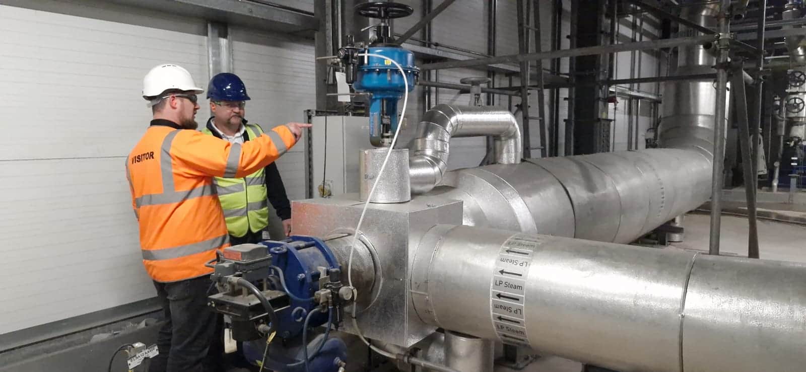 Two engineers inspect industrial piping and machinery at a waste-to-power facility.