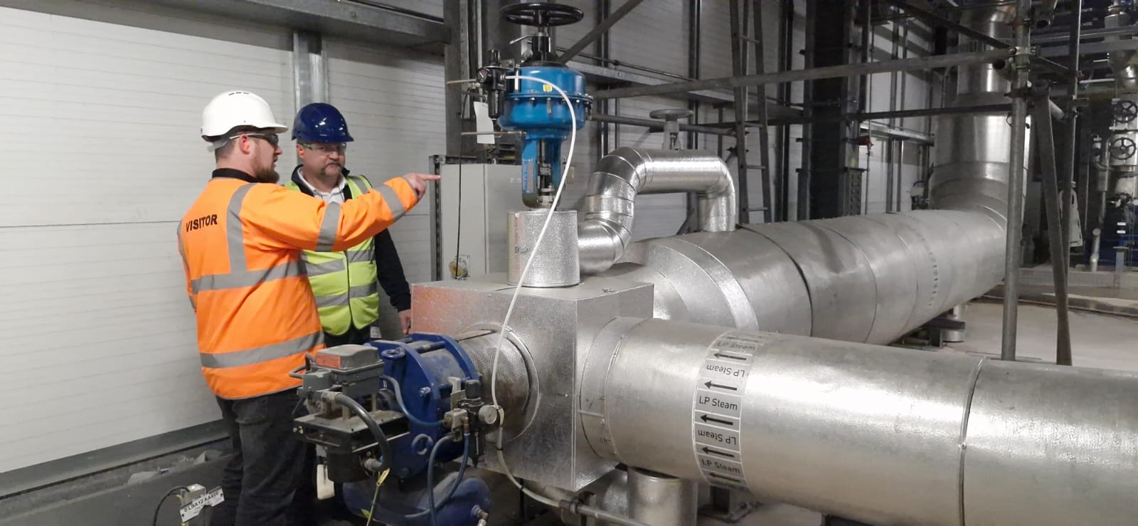 Two engineers inspect industrial piping and machinery at a waste-to-power facility.