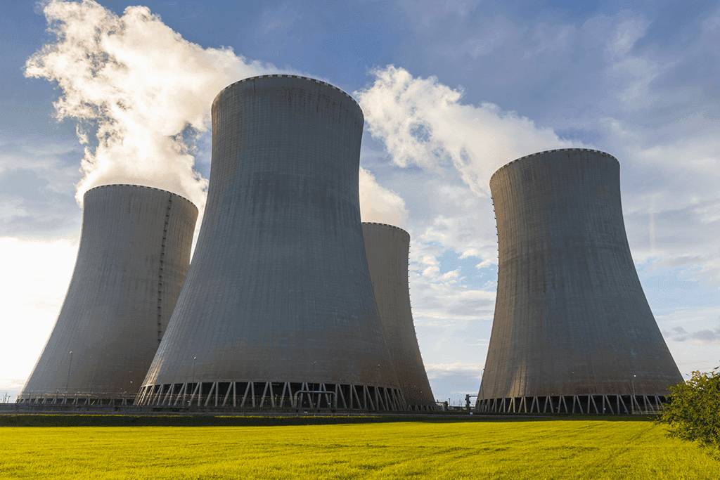 Four nuclear plant cooling towers emitting steam over a green field under a partly cloudy sky.