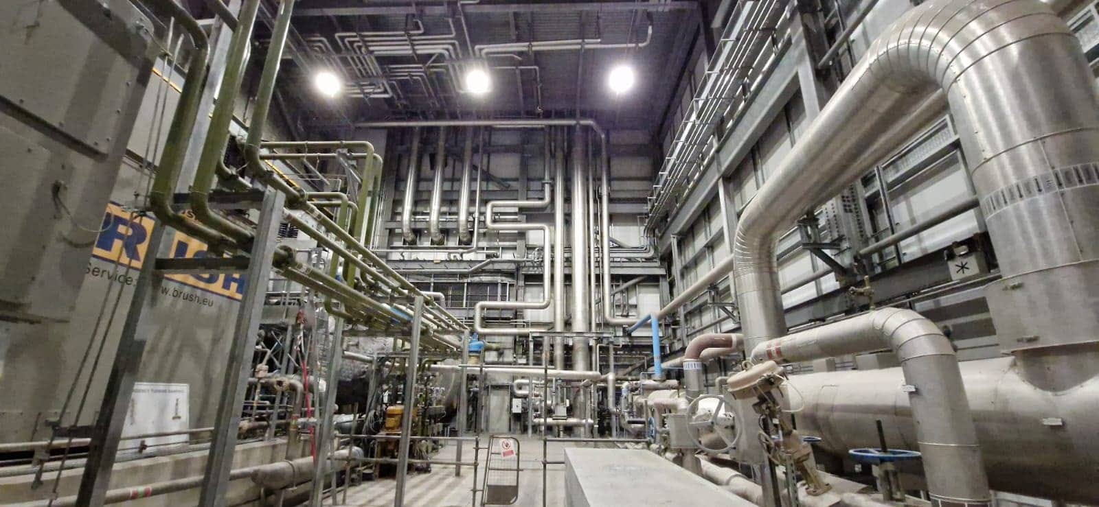 Interior of waste-to-power facility with complex piping and industrial energy conversion equipment.