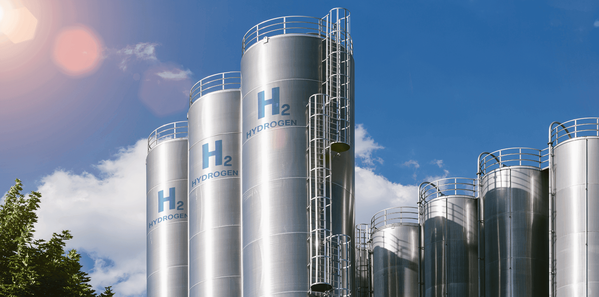 IMI stainless-steel hydrogen storage tanks with H₂ labels and safety railings under a clear blue sky