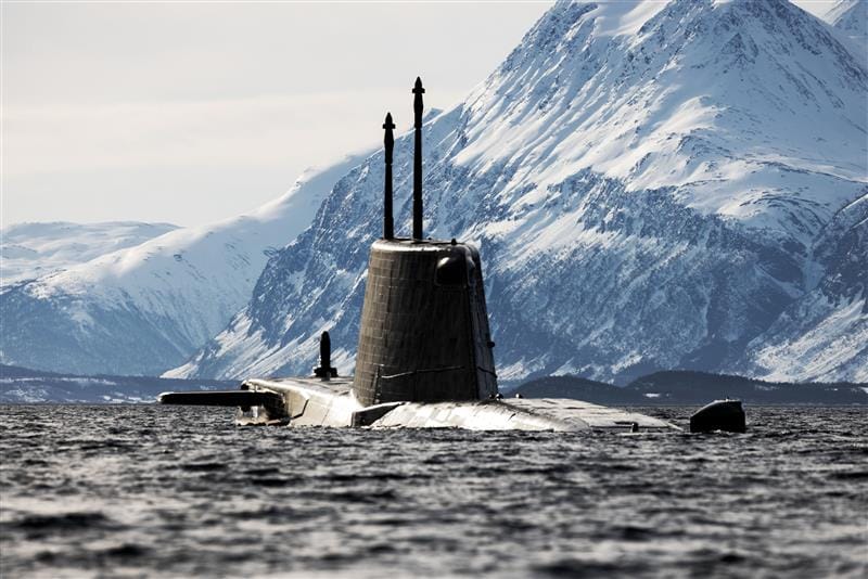Submarine partially submerged with snow-covered mountains in background.