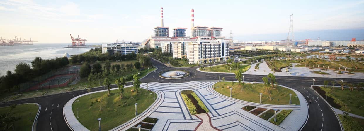 Qinzhou Electric Power Plant with three red-and-white chimneys near a waterfront and landscaped grounds.