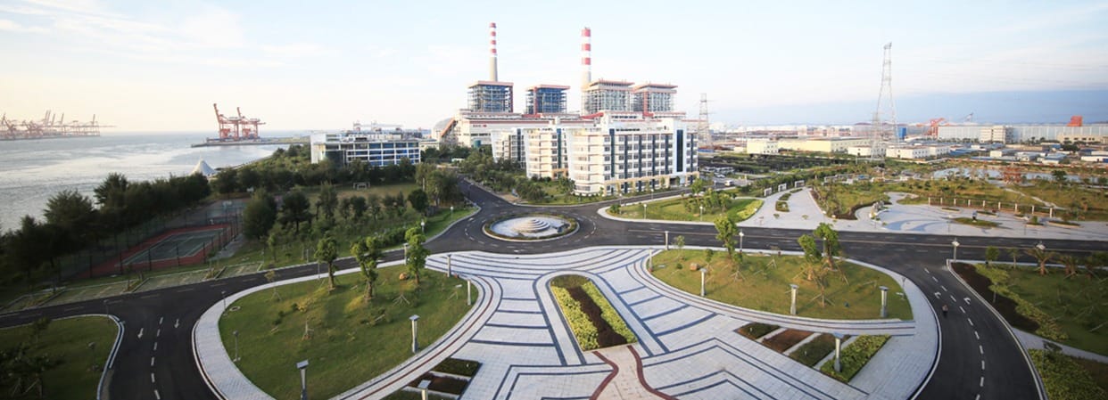 Qinzhou Electric Power Plant with three red-and-white chimneys near a waterfront and landscaped grounds.