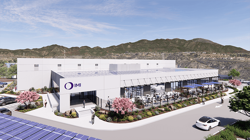 IMI building with large windows, outdoor seating, landscaped grounds, and mountain backdrop.