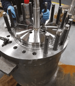 Assembly process showing piston rings being fitted onto a central plug with threaded rods.