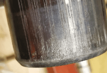 Close-up of worn cylindrical metal part with visible surface damage, indicating non-OEM component failure.