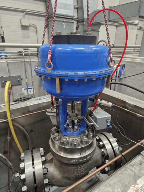 Industrial valve assembly with blue actuator, flanged connections, and attached pipes and cables.