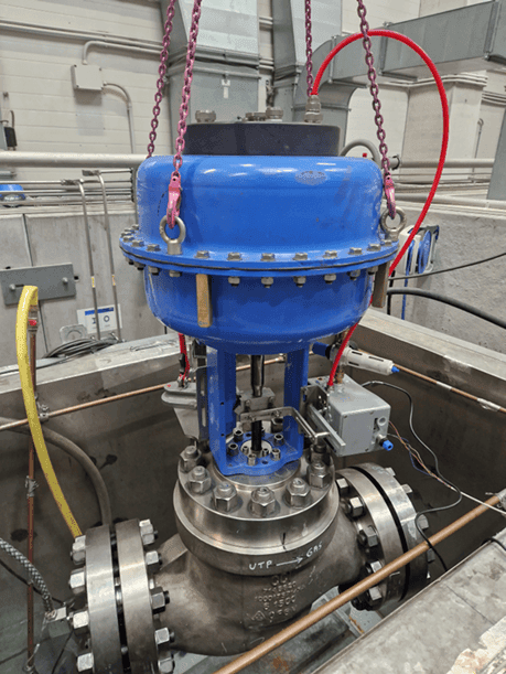 Industrial valve assembly with blue actuator, flanged connections, and attached pipes and cables.
